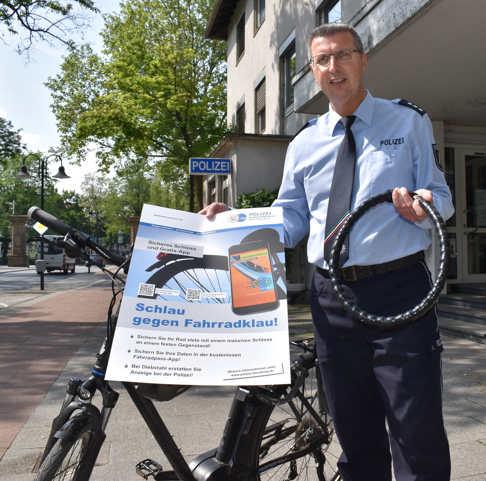 Peter Gall aus der Kriminalprävention der Kreispolizeibehörde Paderborn mit einem Fahrradschloss und einem Hinweis auf die Fahrradpass-App. 